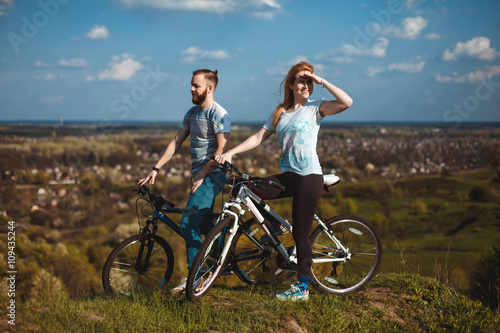 Beautiful young couple in love walking with bicycles, looking towards the beautiful nature and the blue sky. The concept of active rest