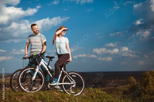 Beautiful young couple in love walking with bicycles, looking towards the beautiful nature and the blue sky. The concept of active rest