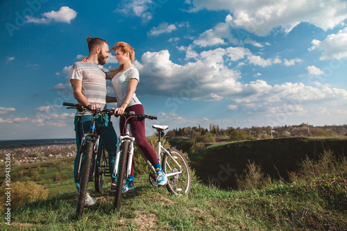 Beautiful young couple in love walking with bicycles hugging and looking at each other. The concept of joy and happiness