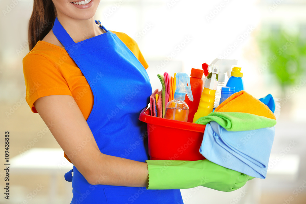 Woman in rubber gloves holding basin with detergents on blurred background Woman in rubber gloves holding basin with detergents on blurred background