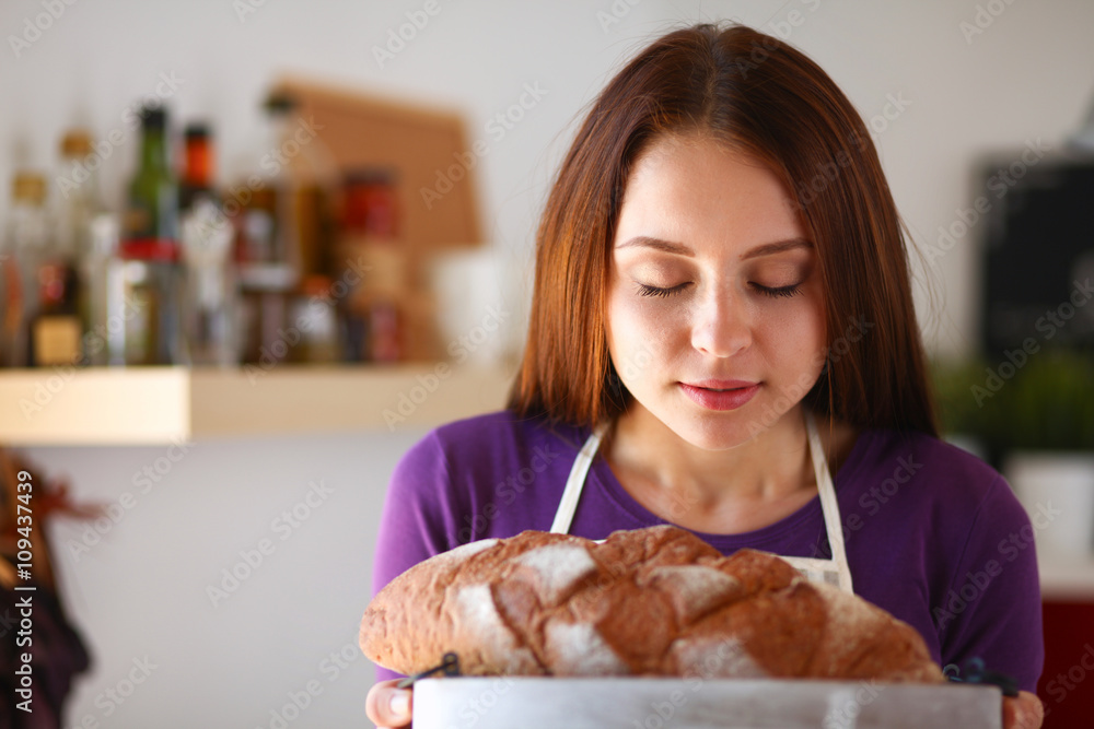 Young woman holding tasty fresh bread in her kitchen Young woman holding tasty fresh bread in her kitchen