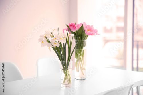 Beautiful tulips and irises on dinning table against white wall background