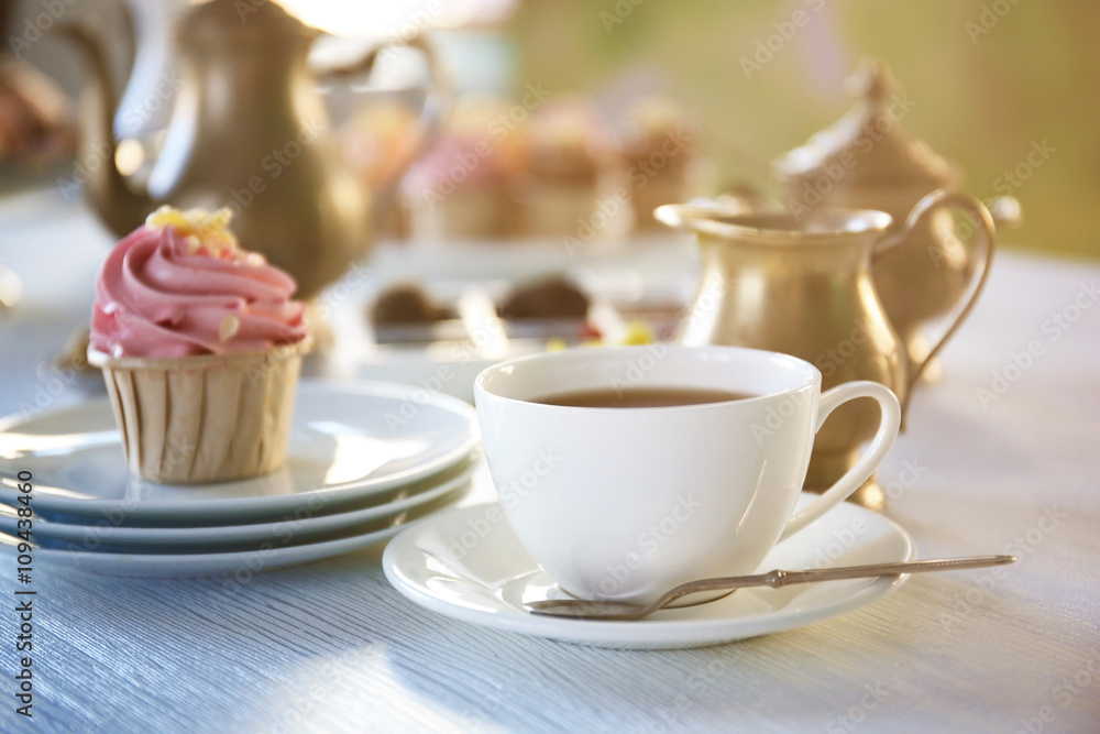 Cupcake with pink cream and cup of tea on wooden table indoors Cupcake with pink cream and cup of tea on wooden table indoors