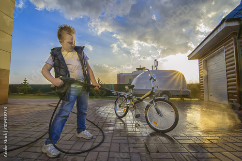 White boy washing his bicycle with the power wash outdoors