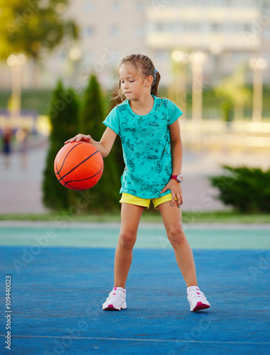 photo of little cute girl playing basketball outdoors