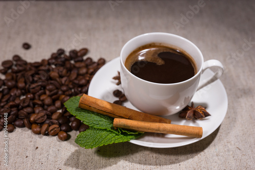 Full cup of coffee with cinnamon sticks and mint