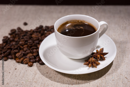 Cup of coffee with spices and beans on tablecloth