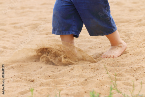 Legs of barefoot of little boy in shorts running on sand
