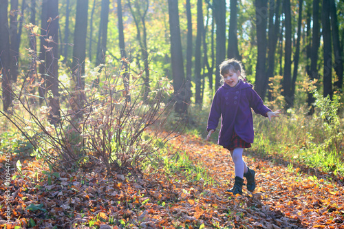 Little beautiful girl in coat runs in park in sunny autumn day