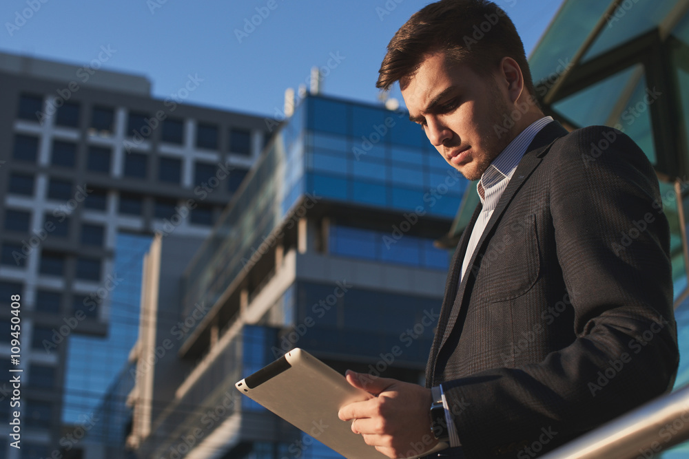 Businessman holding a tablet in hands on the background of buildings with glass facades Businessman holding a tablet in hands on the background of buildings with glass facades