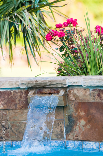Luxurious swimming pool with stone waterfall and pink roses in b