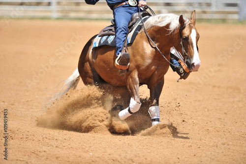 A side view of a rider and horse running ahead in the dust.