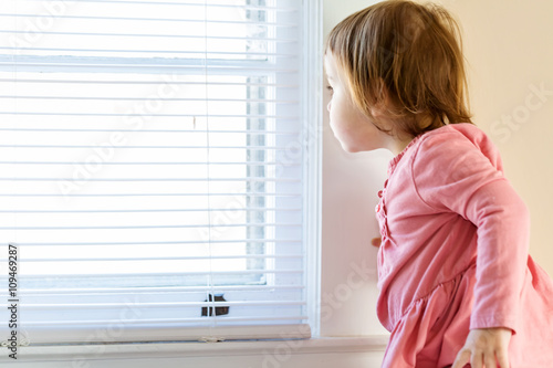 Toddler girl peeking out of the window