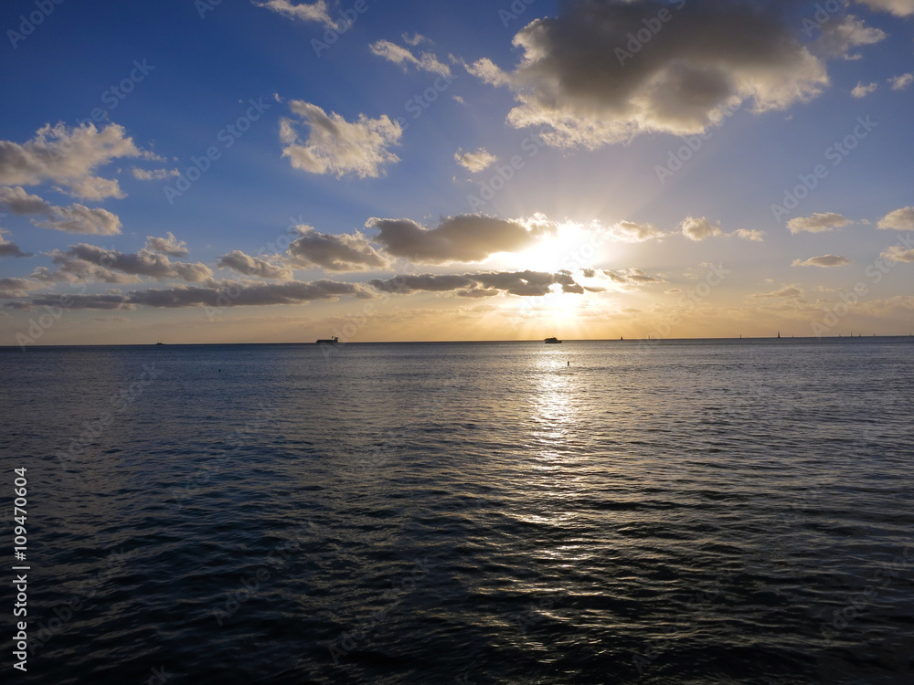 Obraz premium Sunset streams through the clouds with boats on the water