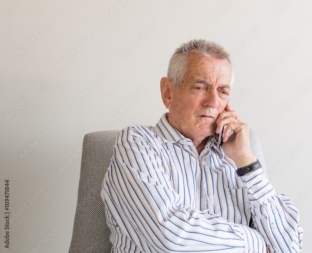 Older man in striped shirt talking on mobile phone and looking concerned Older man in striped shirt talking on mobile phone and looking concerned