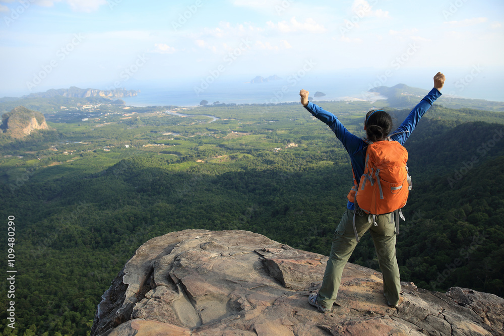 cheering successful woman hiker open arms at mountain peak