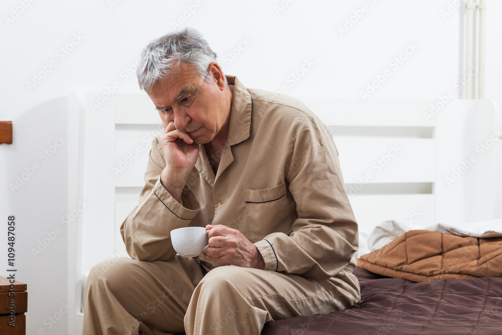 Worried senior man can not sleep. He is sitting on bed and drinking tea. Worried senior man can not sleep. He is sitting on bed and drinking tea.