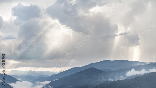 Sun rays light through the clouds in the mountains, dramatic late afternoon scene.