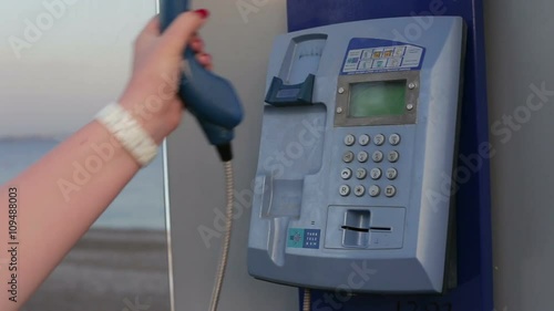 Female hand picks up the phone dials the number of a payphone on the street