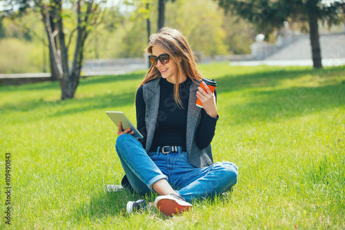 Girl sitting on the grass with coffee and tablet.