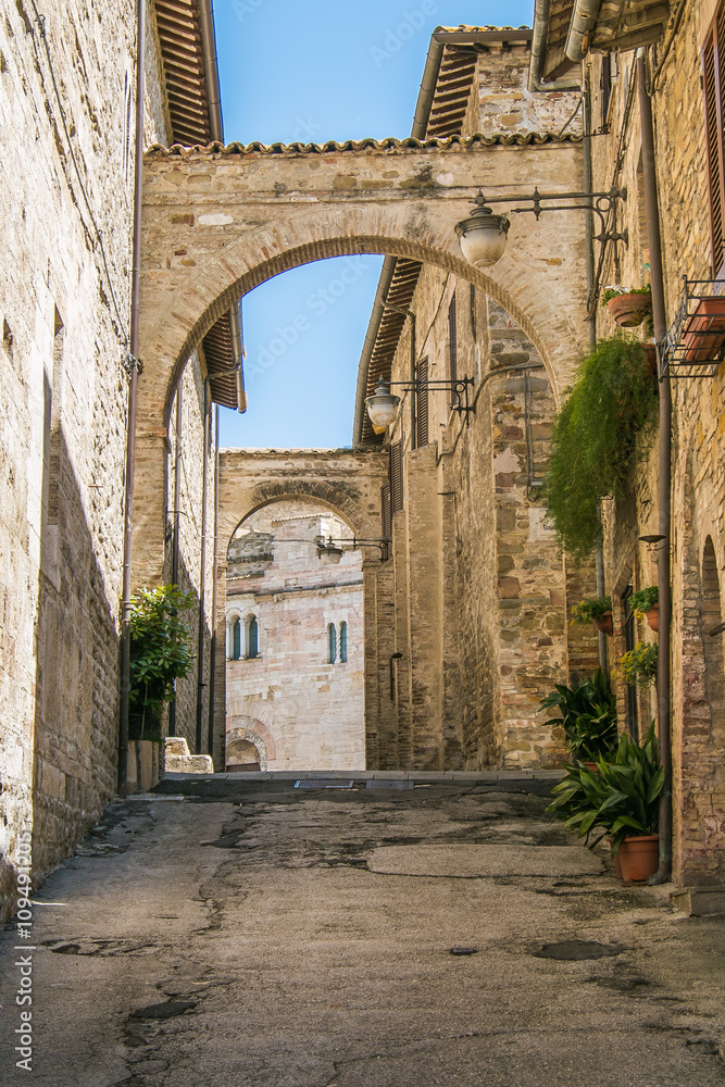 Picturesque narrow alley with ancient arches and pot plants in Bevagna, Umbria, Italy