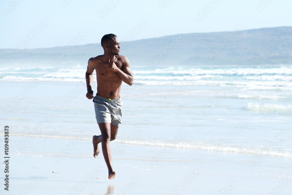 Muscular young african man running along the beach