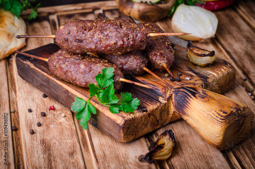 Roasted kebab skewer with spices on cutting board and wooden background. Selective focus