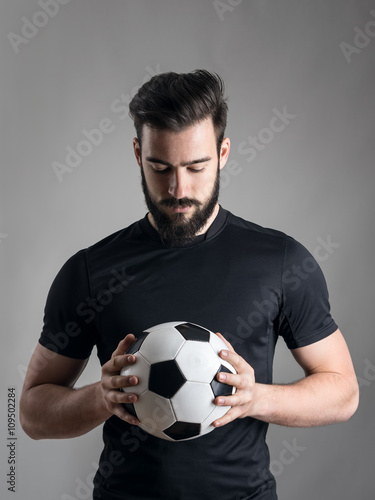 Intense portrait of football player holding and looking at the ball focused over gray studio background. Determination concept.