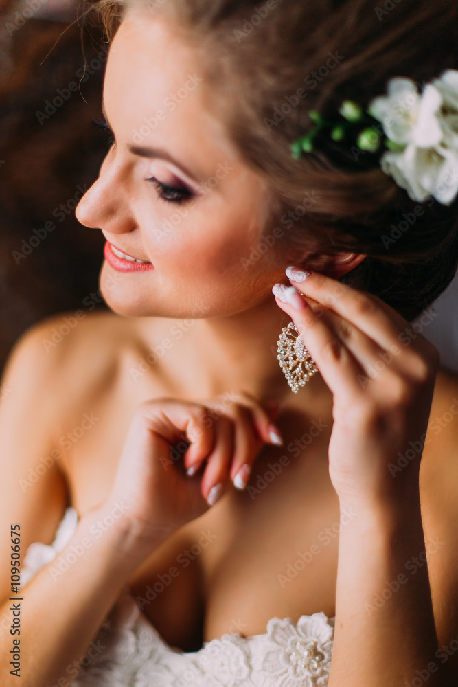 Close-up portrait of beautiful bride in white wedding dress puting on earring