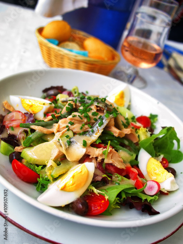 Nicoise Salad served in a restaurant in Cannes, France. Tilted view with rose wine on background