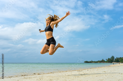Young athletic woman jumping up on a tropical beach 