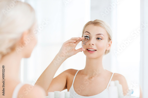 Fototapeta woman with curler curling eyelashes at bathroom