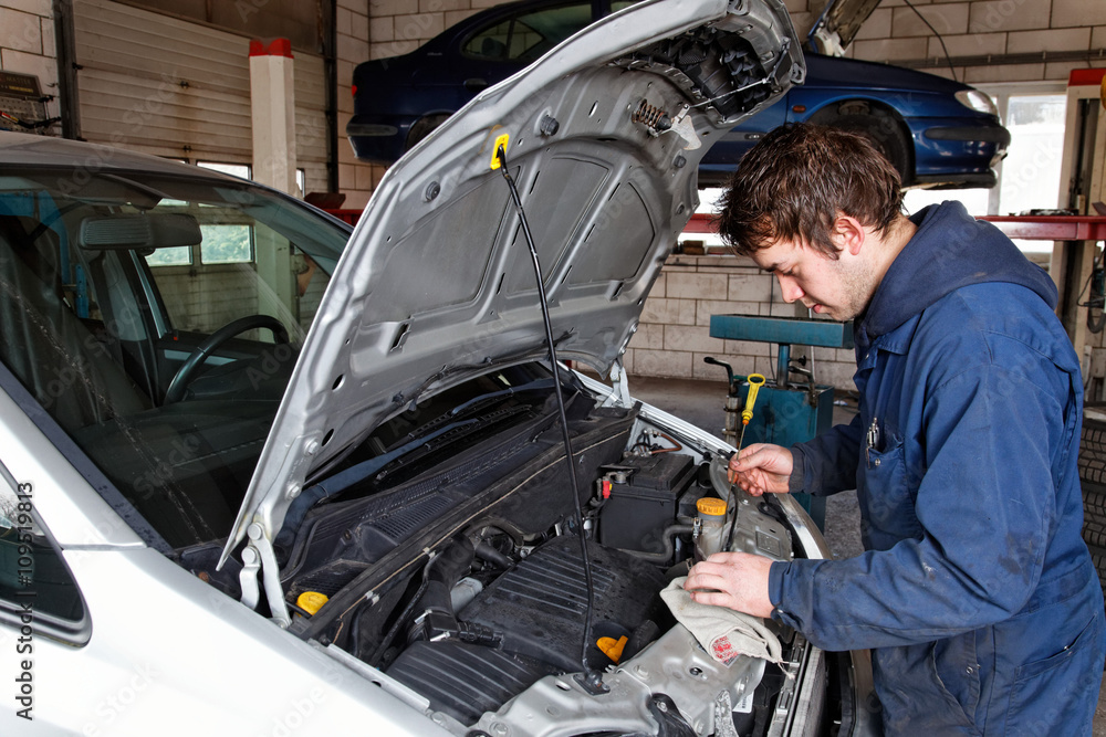 young auto mechanic checks the oil of a car young auto mechanic checks the oil of a car