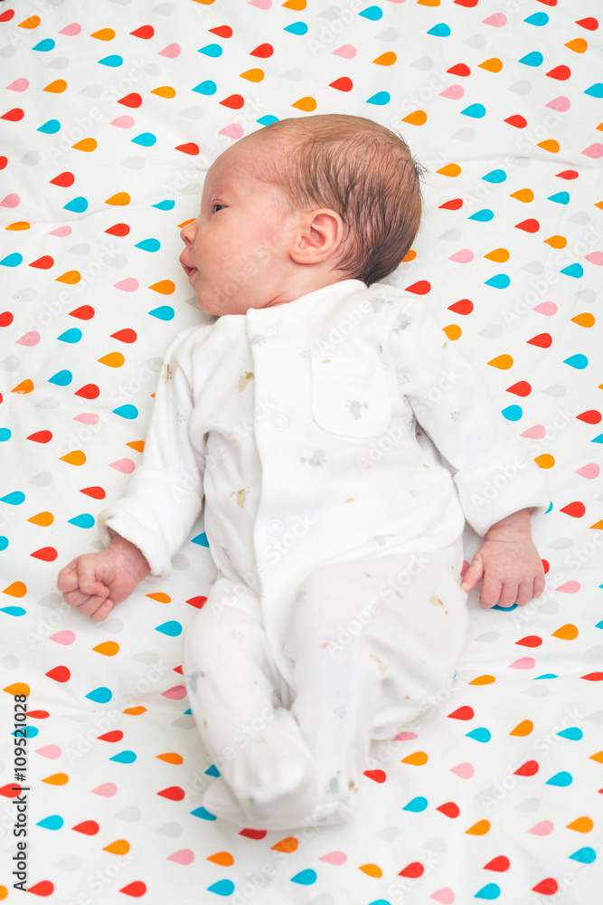 Newborn baby dressed in white sleeping on her back, head to the side