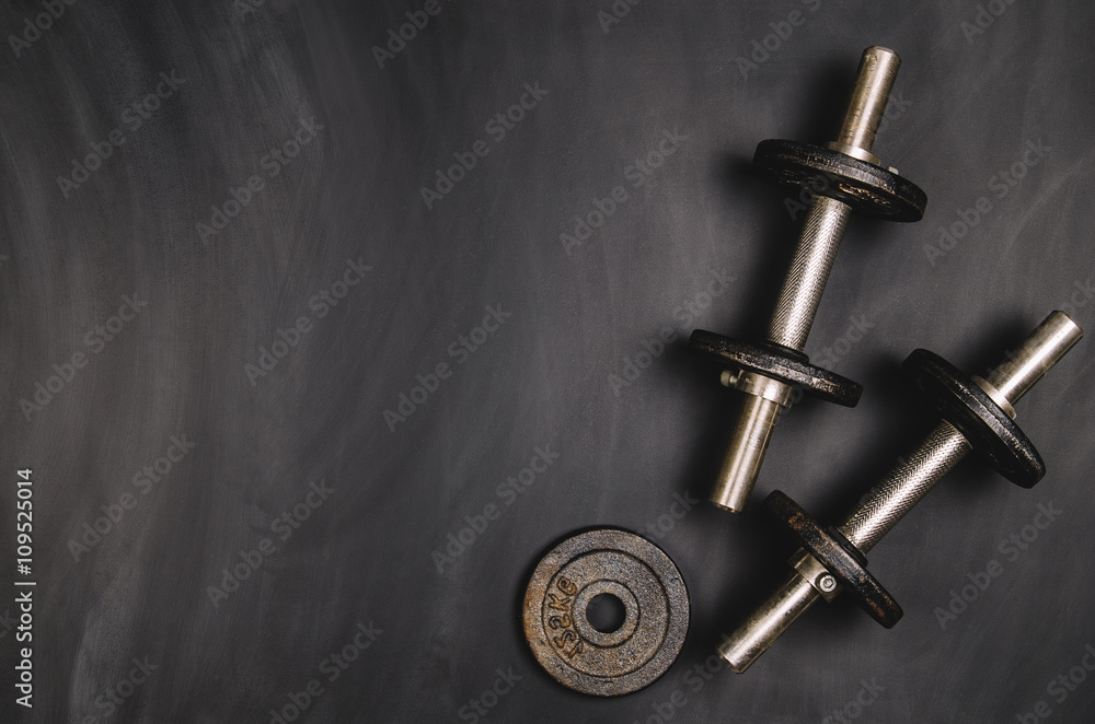 Iron dumbbells on a black chalkboard seen from above. Photo taken from above, top view. Conceptual image background for sport or fitness advertising. Horizontal image. Iron dumbbells on a black chalkboard seen from above. Photo taken from above, top view. Conceptual image background for sport or fitness advertising. Horizontal image.