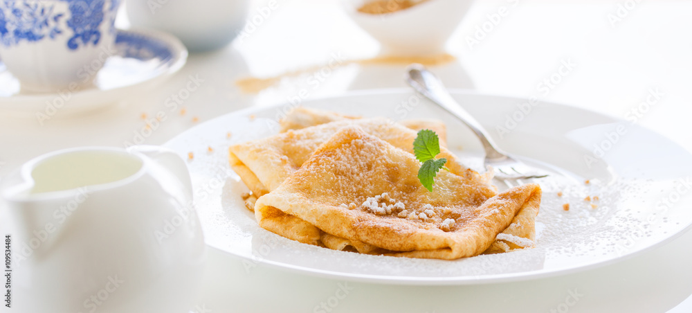 French crepes or pancakes with sugar powder, nuts and fresh mint on a white plate on a white background for breakfast, closeup