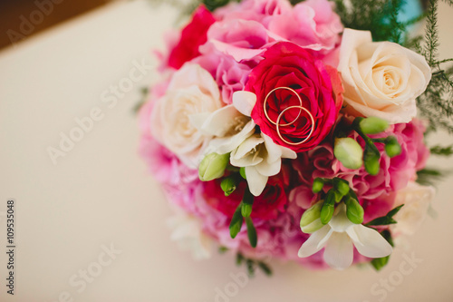 Wedding rings and wedding bouquet of red roses on the table