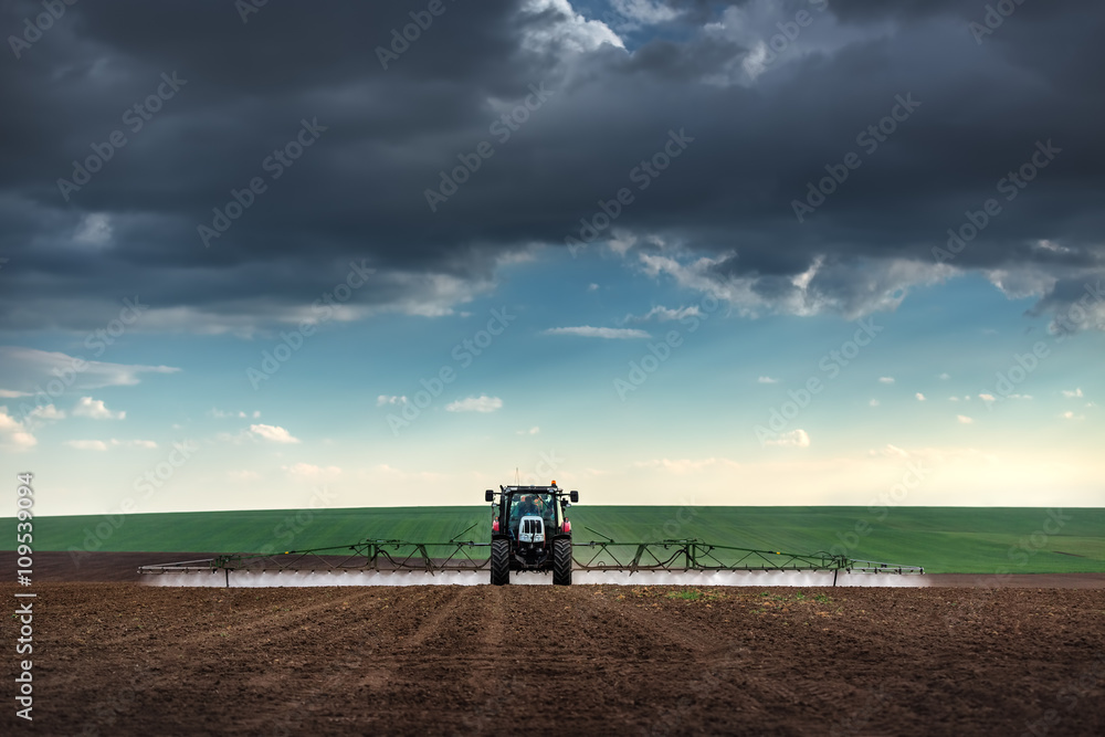 Fototapeta premium Farming tractor plowing and spraying on field