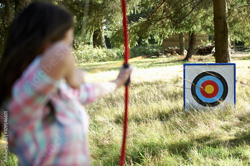 Rear view of teenage girl practicing archery with target photo