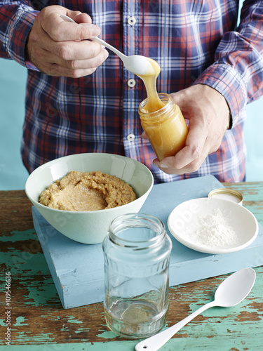 Man preparing fresh mustard recipe step 2, adding honey to blended mustard seeds