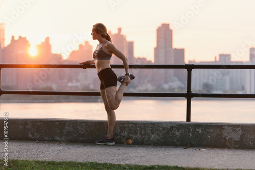 Young woman working out, stretching, by water's edge