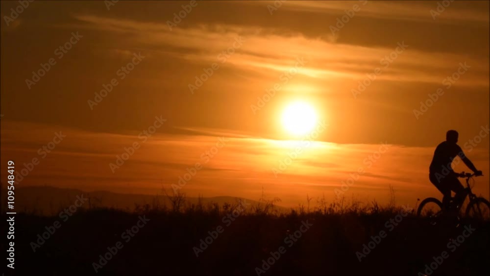 A man riding bicycle on the background of an orange sunset sky, slow motion. Cycling silhouette. Silhouette of man bicyclist against sunset,
A man riding bicycle on the background of an orange sunset sky, slow motion. Cycling silhouette. Silhouette of man bicyclist against sunset,