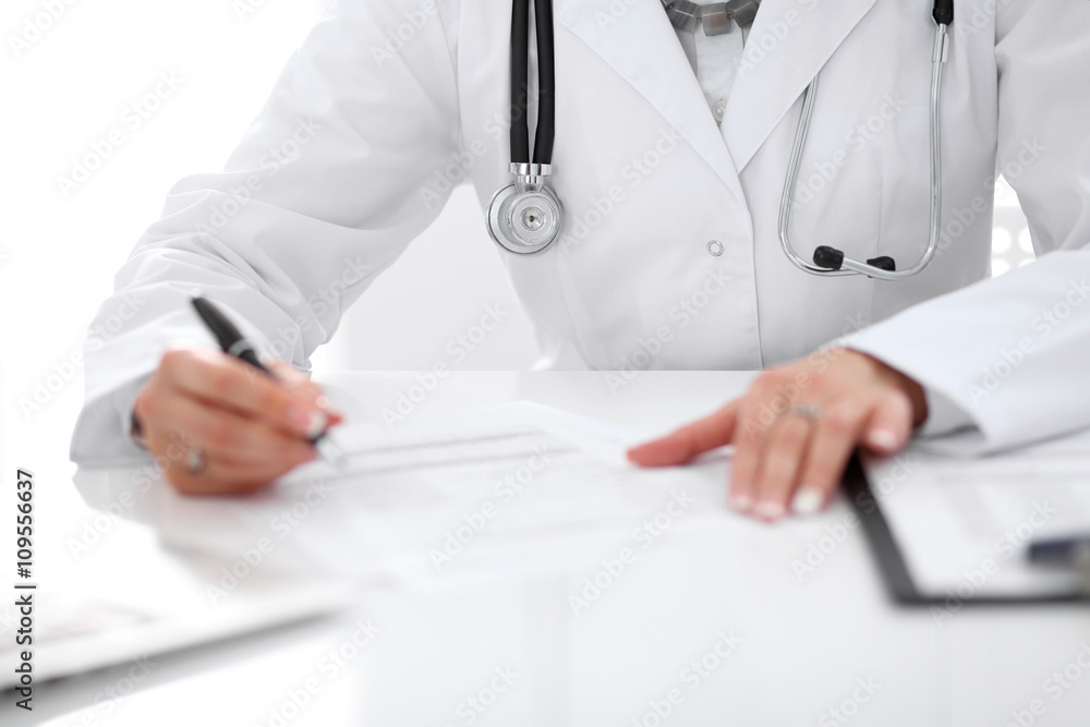 Close-up of a female doctor filling out application form , sitting at the table in the hospital Close-up of a female doctor filling out application form , sitting at the table in the hospital