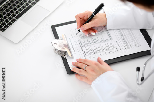 Close-up of a female doctor filling out application form , sitting at the table in the hospital