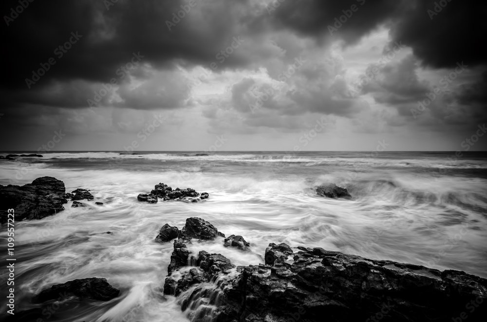 black and white image wave hitting the coastline with dramatic cloud background