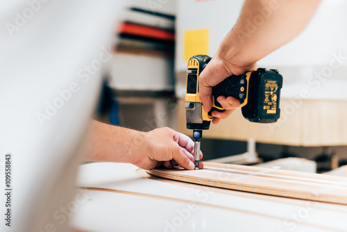 Cropped view of young man in carpentry workshop using cordless screwdriver, screwing into plywood