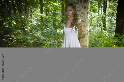 Semi transparent portrait of young woman leaning against forest tree photo