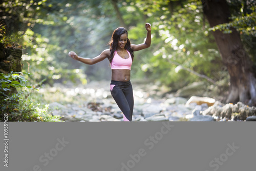 Young female hiker stepping over forest river rocks photo