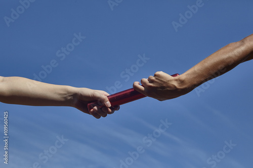 Hands of female relay runners passing baton against blue sky photo