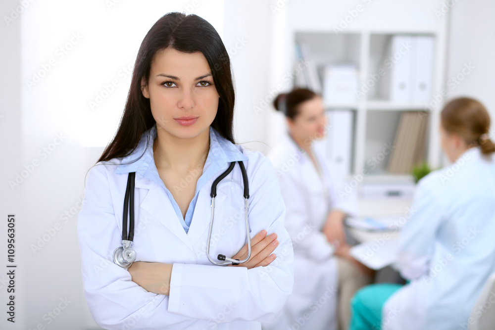 Brunette female doctor on the background of colleagues talking to each other in hospital Brunette female doctor on the background of colleagues talking to each other in hospital